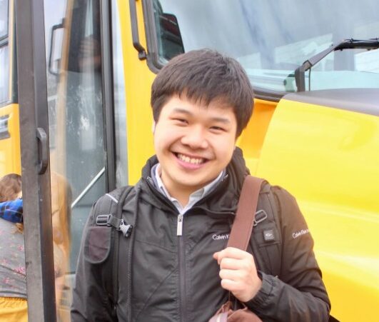 A photo of a person smiling in front of a yellow school bus.